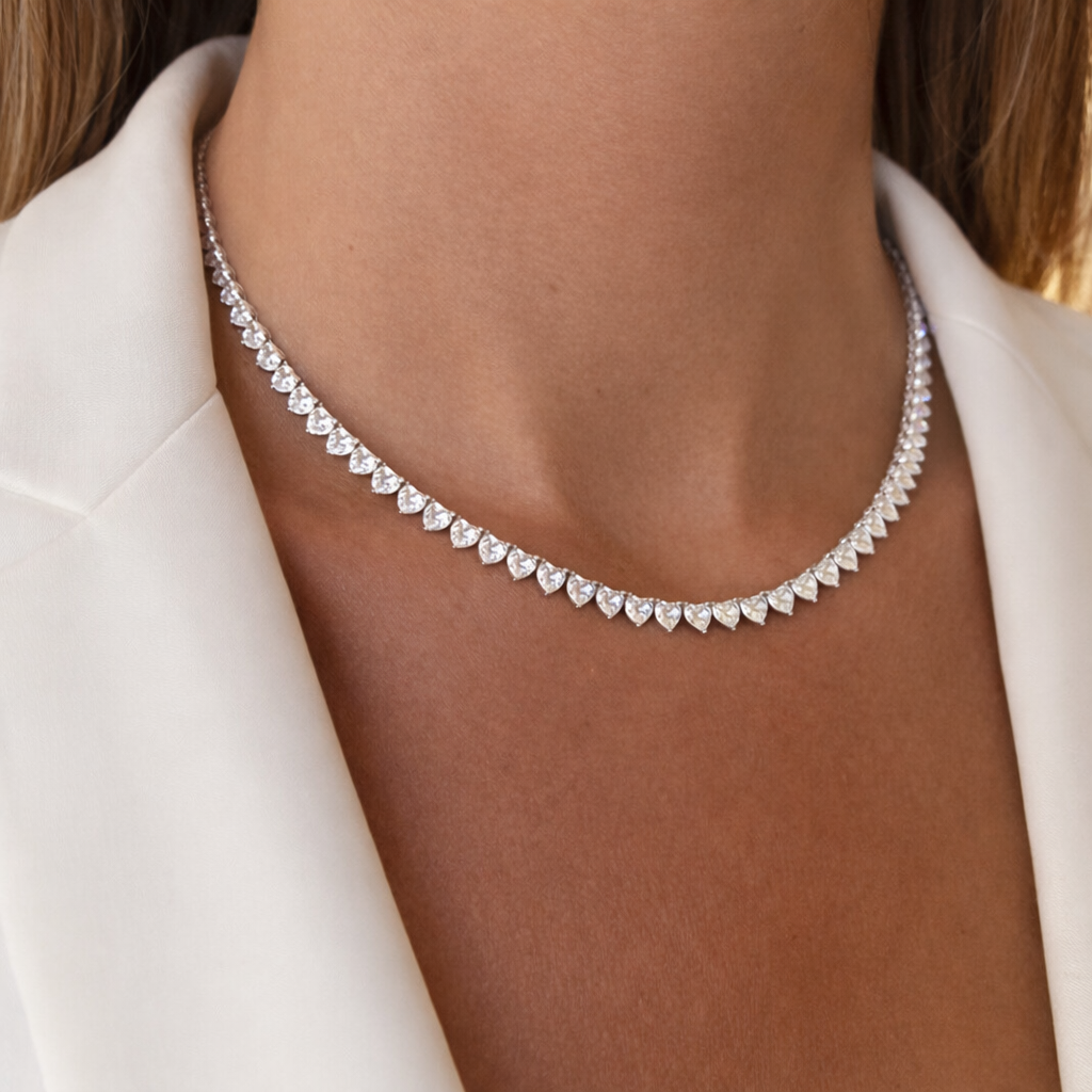 Silver necklace with heart-shaped stones worn by a person against a neutral background