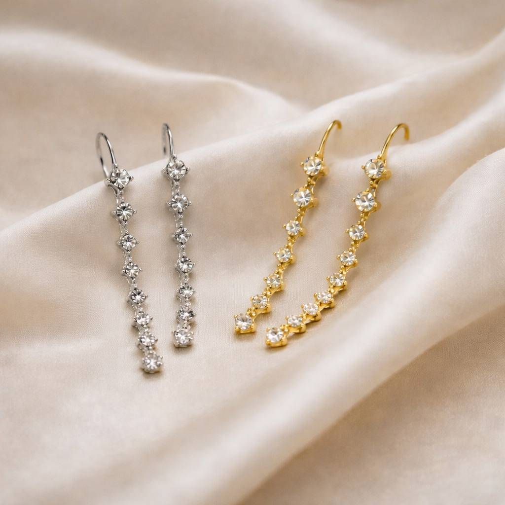 Two pairs of earrings, one gold and one silver, on a beige fabric background.
