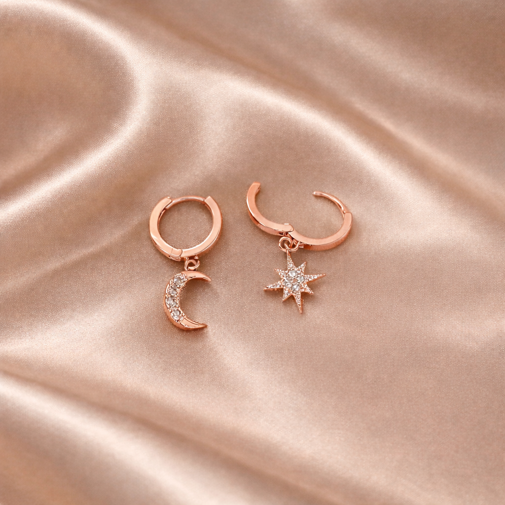 Rose gold hoop earrings with moon and star charms on a pink satin background