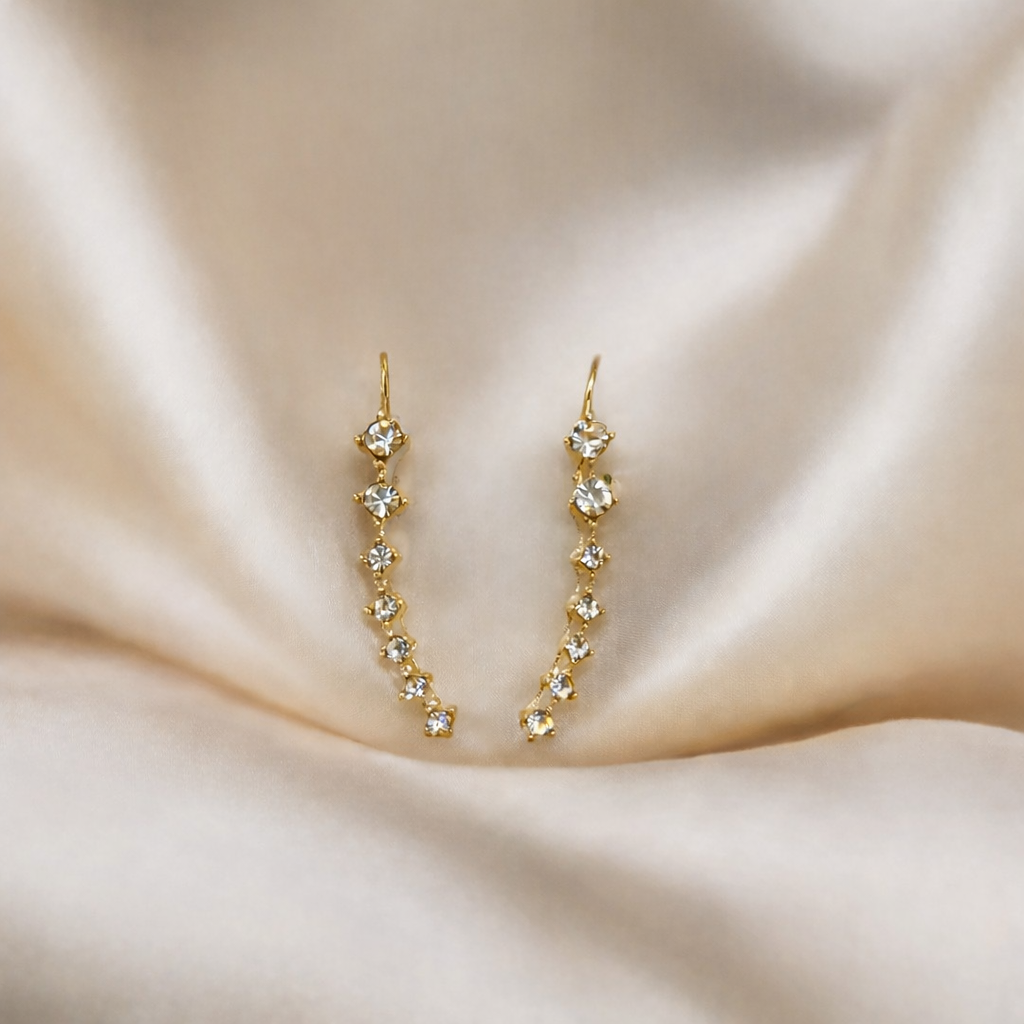 Gold earrings with clear stones on a beige fabric background