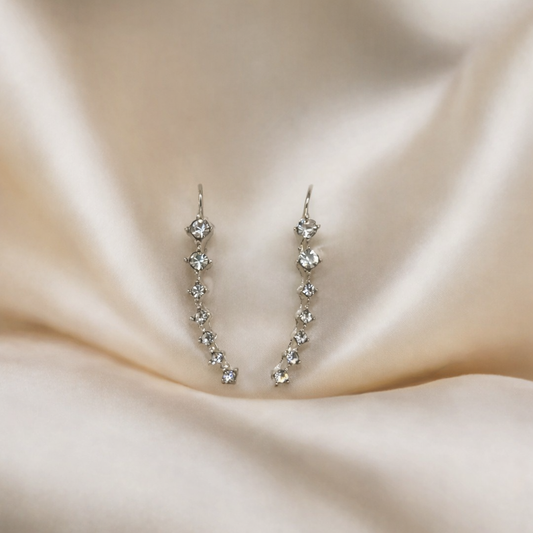 Silver earrings with clear stones on a beige fabric background