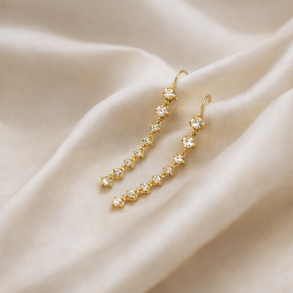 Gold earrings with clear stones on a beige fabric background