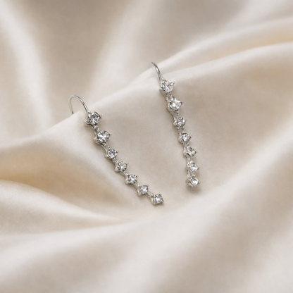 Silver floral earrings on a soft beige fabric background