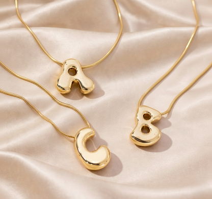 Gold necklaces with letter pendants on a beige fabric background
